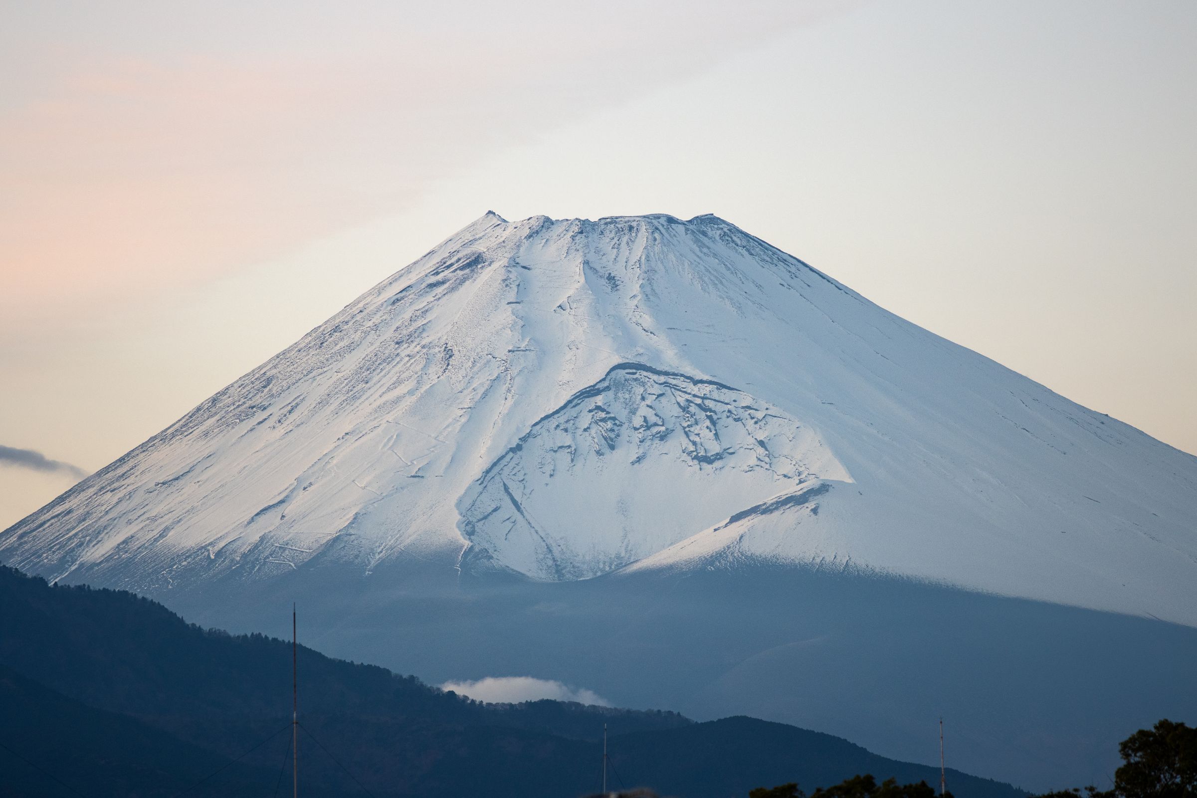 The snow-capped peak of Mount Fuji rising above a ridge under a soft pink sky