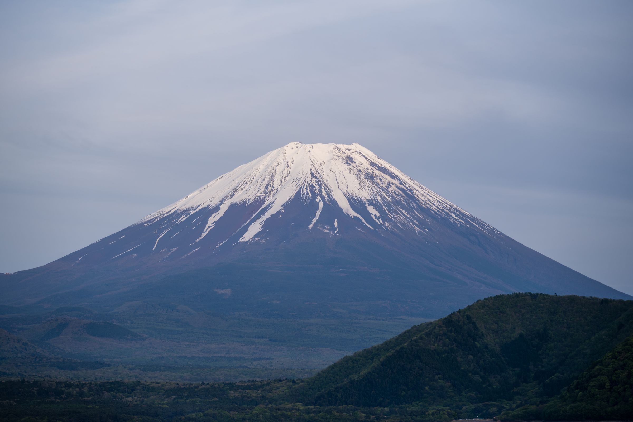 Mount Fuji at dusk above a dark ridge, the sky turning pink behind the cone